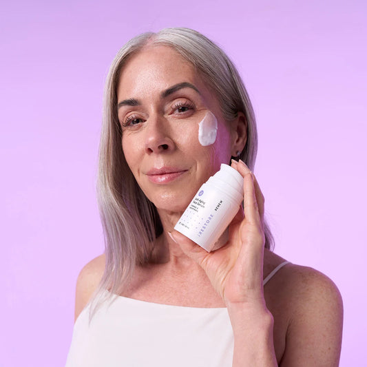 Mature woman with anti-aging face serum on her face while holding the bottle on her hand