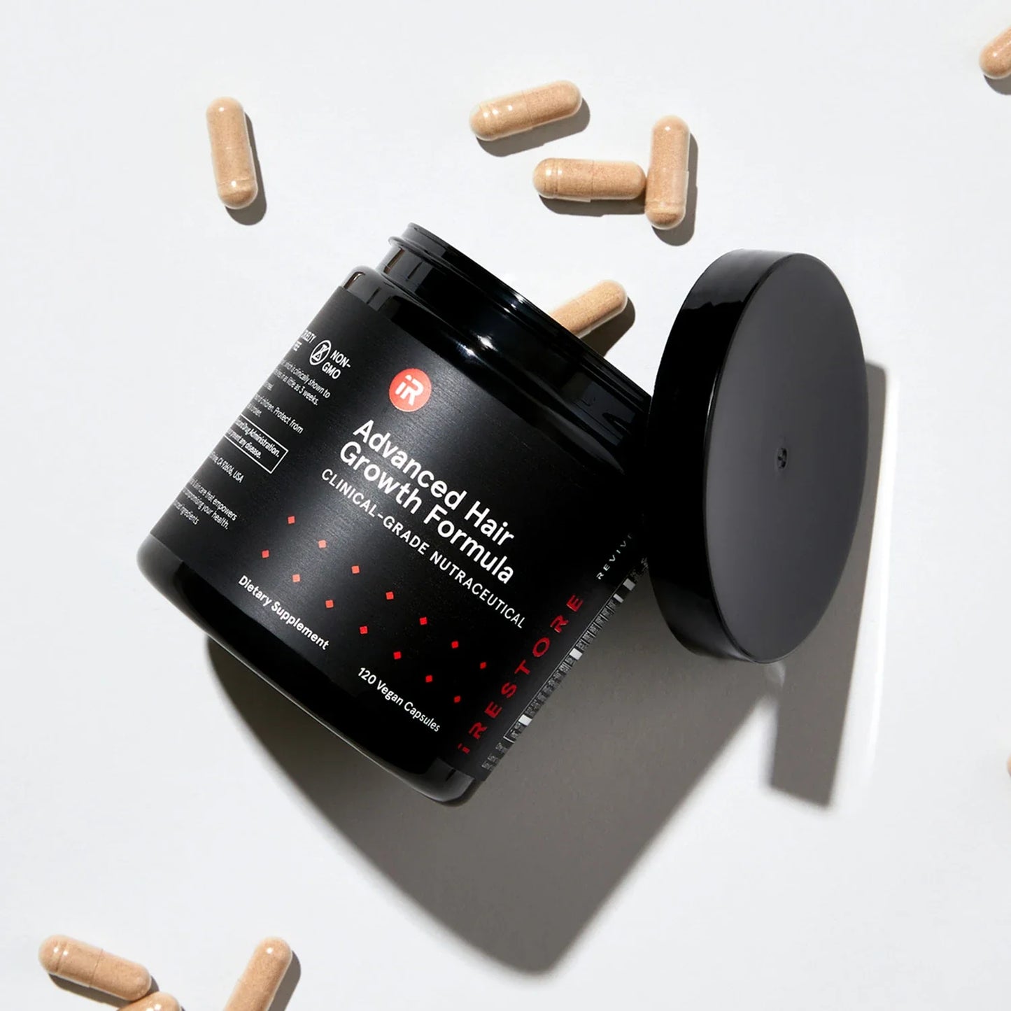 Top view image of an opened jar of the Advanced Hair Growth Formula tipped on its side with spilled tablets around it.