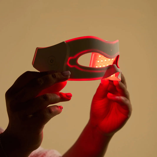 Close up shot of as woman's hand holding up the LED eye mask with the red lights tuned on.