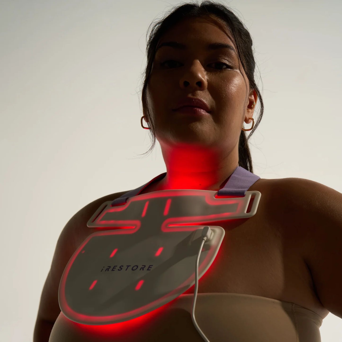 Woman in mild silhouette wearing the iRESTORE LED neck and chest mask, with the red LED light turned on